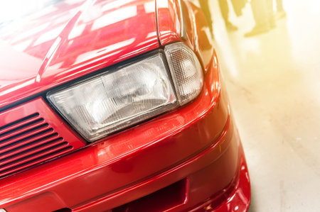 Closeup on headlight of a red car in the sunlight