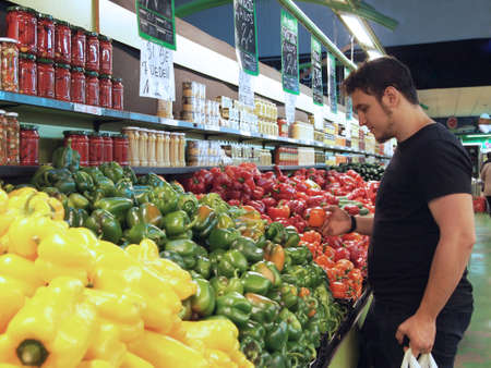 Latin young man looking at the peppers in a greengrocery store, Madrid, Spain.の写真素材