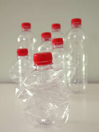 Red cap plastic bottles order by size on a green back ground. The smaller one is in the middle, the others are "looking" at it. Recycle concept.の写真素材