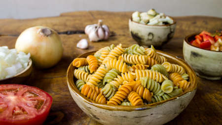 Fresh ingredients for cooking: pasta, tomato, red pepper, onion, eggplant and garlic over wooden table background.の写真素材