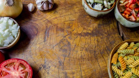 Fresh ingredients for cooking: pasta, tomato, onion, red pepper, eggplant and garlic over wooden table background with copy space. Top view.の写真素材
