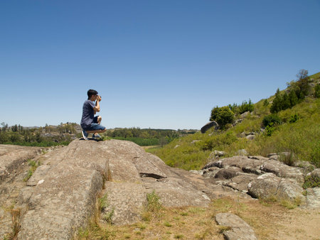 Young argentinian photographer taking a picture at the top of a rock. Photography, shooting concept.