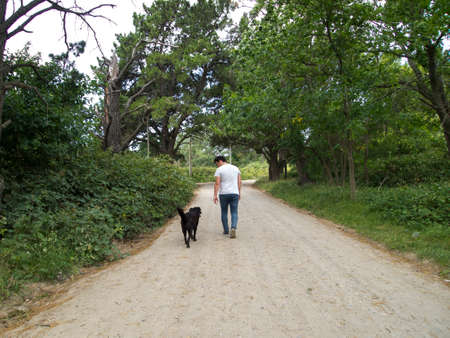 Young man looking to a black labrador dog, while both walking on a path, Tandil, Buenos Aires, Argentina.の写真素材