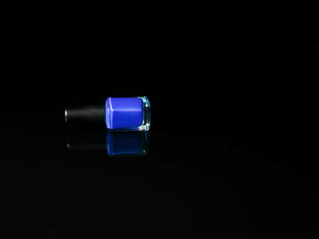 Blue nail polish bottle lying on black background with refection. Beauty and cosmetic concept.の写真素材
