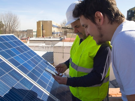 Caucasian seasoned technician showing the app to his young client beside the solar panels....