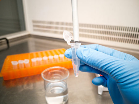 Lab technician in blue medical gloves using an electronic pipette to put liquid in an eppendorf....