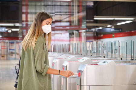 Young woman wearing face mask, entering through the train station turnstiles. Public transport concept.の写真素材
