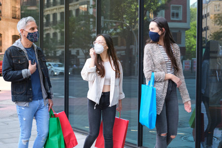 Three friends wearing face mask talking and walking on street carrying shopping bags. Shopping...