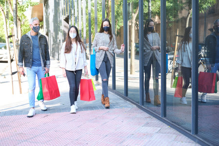 Three friends wearing face mask walking on street with shopping bags. Shopping during pandemic...