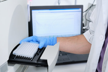 A researcher putting PCR plate on the thermal cycler for DNA amplification. Curve chart on monitor...