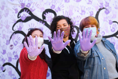 Three women with their hands painted purple participating in the International Day for the Elimination of Violence against Women participatory mural. 25 november.の写真素材