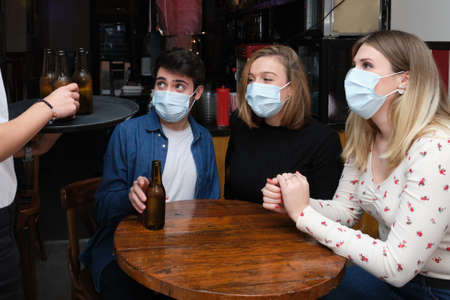 Waitress bringing drinks to her customers wearing protective face masks. New normal in bars.の写真素材