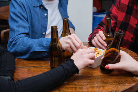Unrecognizable four friends drinking and eating snacks in a pub. Friendship concept.の写真素材
