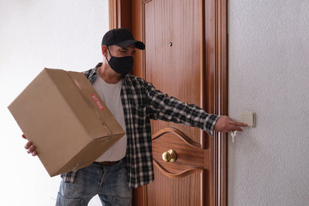Delivery senior man ringing the door bell holding a package. "Muy fragil" means very fragile. Delivery service under quarantine, disease outbreak, coronavirus covid-19 pandemic conditions.の写真素材