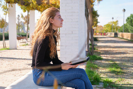 Redhead caucasian woman reading or working in a e-book or tablet in a park. Digital nomad entrepreneur concept.の写真素材