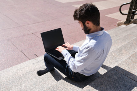 Young business man using his laptop sitting on stairs. Businessman in a urban street of a city.