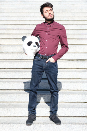 Young business man with a panda head mask in his hands, standing on stairs. Bizarre businessman.
