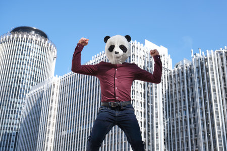 Young business man wearing a panda head mask, strong in front of the corporate buildings. Bizarre businessman.の写真素材
