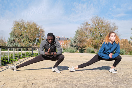 African black man and redhead caucasian woman stretching their legs in a park. Fitness and sport outdoor.の写真素材