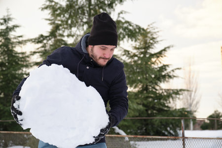 Young caucasian man carrying a big snowball to make snowman during Filomena snowstorm in Madrid, Spain. Winter activities.の写真素材