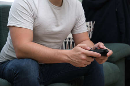 Unrecognizable young man playing video games with a gamepad sitting on sofa. Gamer at home.の写真素材