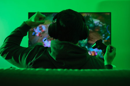 Unrecognizable gamer wearing headphones, celebrating a victory in video games in from of the...