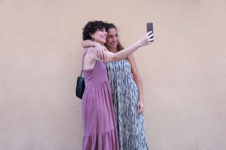 Beautiful lesbian couple wearing long dresses taking a selfie in the street. Young woman friends.の写真素材