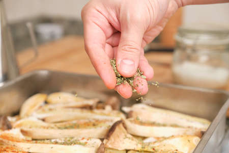 Closeup of man hands adding oregano over sliced king trumpet mushrooms (pleurotus eryngii), potatoes and onions. Cooking process. Mediterranean diet.の写真素材