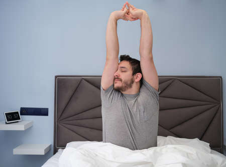 Young latin man stretching in bed after sleeping. Late in the morning.の写真素材