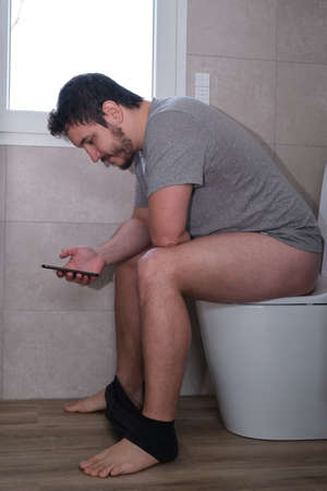Young latin man with his smartphone sitting on the toilet.の写真素材