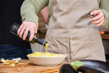 Unrecognizable young woman pouring olive oil on sliced potatoes. Cooking time.の写真素材