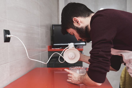 Young caucasian man in apron cooking in a kitchen. He is using a blender.