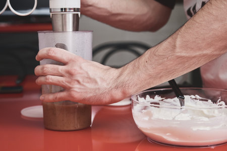 Unrecognizable young caucasian man in apron washing using a blender in a kitchen. He is preparing a cake.の写真素材