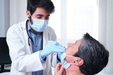 Mature woman getting PCR test at doctor's office during pandemic. Doctor wearing gloves and mask doing the nasal test.の写真素材