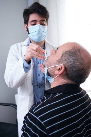 Mature man getting PCR test at doctor's office during pandemic. Doctor wearing gloves and mask doing the nasal test.の写真素材