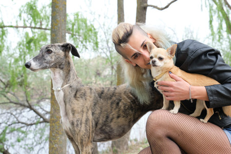 Young punk woman with her dogs in a park. Greyhound and chihuahua dogs.