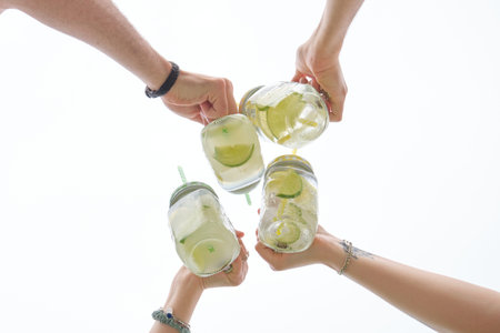 Group of four unrecognizable friends toasting with refreshing drinks over white sky background.の写真素材