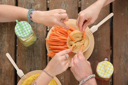 Group of unrecognizable happy friends taking hummus with carrot sticks in a park having picnic on a sunny summer day. Top view.の写真素材
