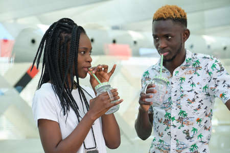 Stylish african couple drinking refreshing drinks at street. Summertime concept.の写真素材