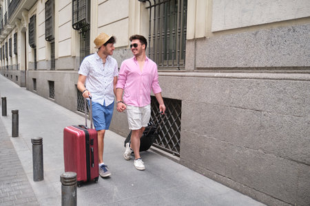 Gay couple carrying suitcases and going to the hotel holding hands.の写真素材