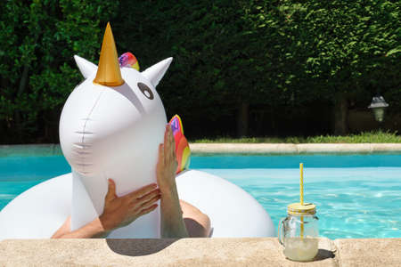 Young man hands touching a unicorn inflatable ring in a swimming pool. Summer concept.の写真素材
