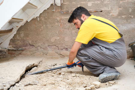 Young caucasian construction worker breaking up a house floor with a crowbar.の写真素材