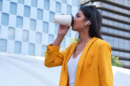 Young latin businesswoman drinking coffee and listening music outdoor.の写真素材