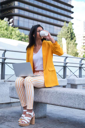 Young latin businesswoman drinking coffee and working with a laptop outdoor.の写真素材