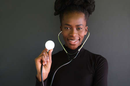 Portrait of smiling female african doctor using the stethoscope in a black background. Studio shot.の写真素材