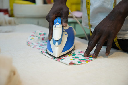 Unrecognizable tailor ironing fabric in his sewing shop. African man working in a workshop.