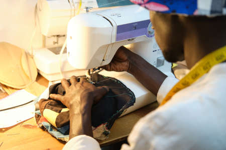 African tailor sewing a hat with sewing machine at sewing workshop. Black man working with african fabrics.の写真素材