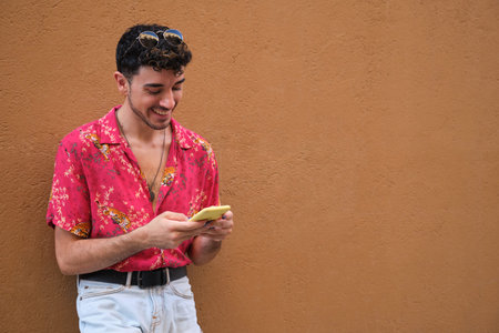Young caucasian man with long false nails smiling and chatting on the smartphone on a brown wall.