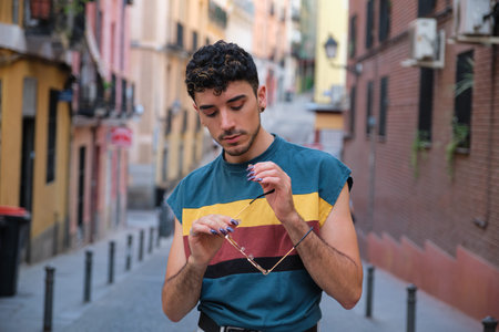 Young caucasian man with long false nails posing with his sunglasses looking down at street.