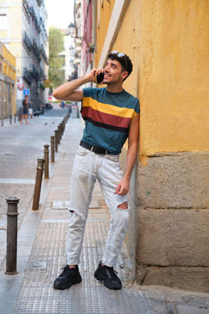 Young caucasian man with long false nails smiling and speaking on the smartphone, standing against a yellow wall.の写真素材